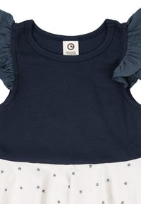 Námořnický proužkovaný top s nařasenými rukávy přechází do bílé sukně zdobené malými modrými květinovými vzory. Je možné vidět štítek uvnitř.