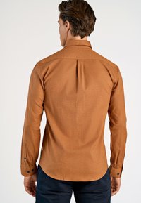 Brązowa koszula z długimi rękawami, z kołnierzem, plisą z tyłu i mankietami zapinanymi na guziki; wykonana z teksturowanej tkaniny o gładkim wykończeniu.