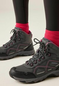 Black and gray waterproof hiking boots with pink accents and black-and-white laces worn with bright pink socks and black leggings.
