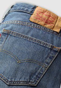 Gros plan de la poche arrière d'un jean en denim bleu avec des coutures jaunes et une étiquette en cuir usée Levi Strauss & Co. au-dessus de la poche.
