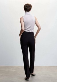 Maglione a collo alto in materiale a coste grigio chiaro abbinato a pantaloni neri sartoriali, caratterizzati da una consistenza liscia e una silhouette aderente.