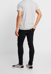 Camiseta gris de manga corta, jeans negros ajustados y zapatillas Vans a cuadros en blanco y negro. Diseño simple sin patrones visibles.