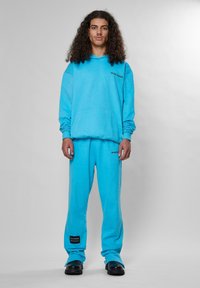Sudadera turquesa y pantalones de chándal a juego, hechos de una tela suave, con un bolsillo frontal y acentos de logo en negro. Textura suave, ajuste relajado.