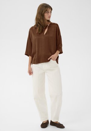 Braune Satinbluse mit schmalem Ausschnitt, lockerer Passform und kurzen Ärmeln, kombiniert mit weißen, schmal zulaufenden Hosen und dunkelbraunen Schuhen.