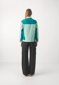 Giacca color block in turchese e blu chiaro con maniche lunghe e colletto, abbinata a pantaloni cargo neri a gamba larga. Design casual con tasche.