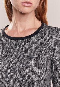 T-shirt à manches longues en motif chevron noir et blanc texturé, avec un col rond noir et une finition en tissu doux.
