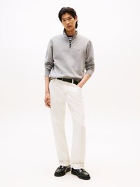 Sweatshirt zippé gris, chemise rayée en dessous, pantalon blanc, ceinture noire et chaussures noires. Design simple et épuré sur un fond neutre.