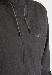 Veste grise en tissu texturé, avec capuche ajustable à cordons et logo imprimé sur la poitrine. Design fonctionnel et minimaliste.