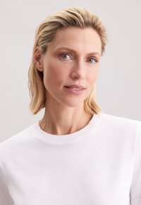 Wit katoenen T-shirt met een klassieke ronde hals. De textuur is zacht met een gladde afwerking, geplaatst tegen een neutrale achtergrond.