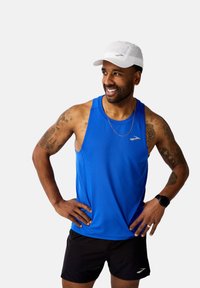 Blå träningslinne med rund halsringning, lättviktsmaterial, tillsammans med svarta shorts. En vit keps och handledsur avslutar outfiten.