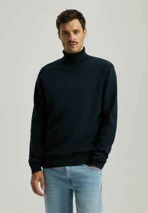 Ciemnoniebieski sweter typu golf w miękkiej dzianinie, z subtelnym logo na klatce piersiowej, długimi rękawami oraz ściągaczem przy kołnierzu i dole.