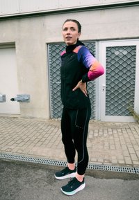 Fekete sportdzseki színes ujjal, fekete leggings-szel, amely fényvisszaverő részletekkel rendelkezik, és fekete sportcipő, menta színű akcentussal.