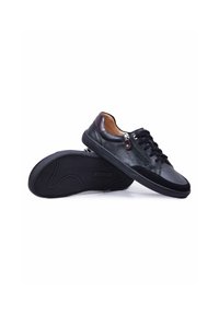 Paire de baskets basses en cuir noir avec lacets et fermeture éclair latérale, une chaussure reposant sur sa semelle, l'autre sur le côté.