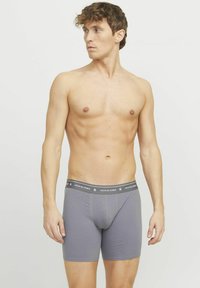 Graue Boxershorts aus weichem Material, mit einem elastischen Bund, der ein Logo trägt, sowie einer figurschmeichelnden Passform, die Unterstützung bietet.