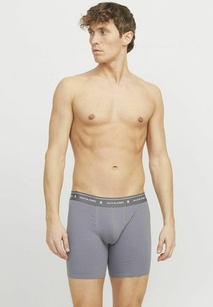 Graue Boxershorts aus weichem Material, mit einem elastischen Bund, der ein Logo trägt, sowie einer figurschmeichelnden Passform, die Unterstützung bietet.