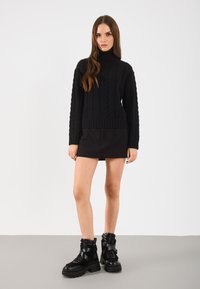 Fekete kabelhorgolt garbós pulóver fekete mini szoknyával és vastag talpú, texturált részletekkel ellátott fekete bokacipővel párosítva.