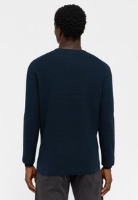 Marinblå stickad tröja med ribbad textur, långa ärmar och rund halsringning. Synlig sömnad längs fållen och manschetterna.