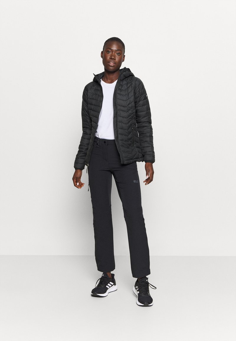 Chaqueta acolchada negra con capucha, combinada con pantalones negros y zapatillas negras. La parte superior cuenta con un cierre y bolsillos laterales. Camiseta blanca debajo.