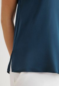 Navyblå blus med en slät yta, med sidokilar och rak fåll. Den är stylad mot en ljus bakgrund.