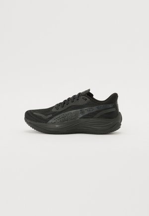 Black athletic shoe with a textured mesh upper, flat laces, and a cushioned sole featuring subtle reflective accents.