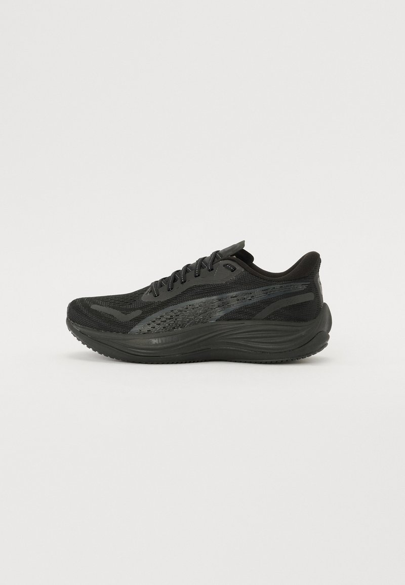 Chaussure de sport noire avec une tige en mesh texturé, des lacets plats et une semelle rembourrée dotée de subtils accents réfléchissants.