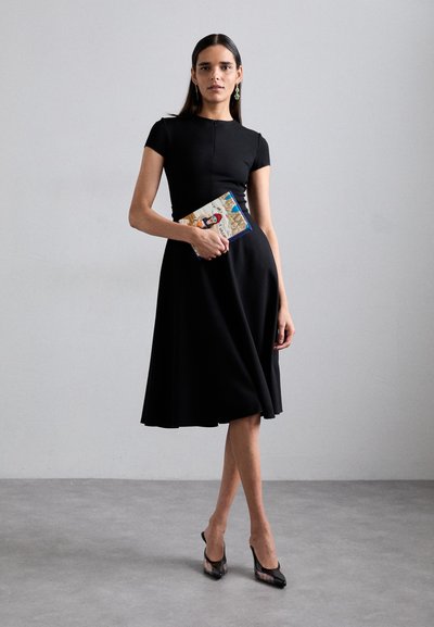 Rochie neagră cu mânecă scurtă, cu un corset ajustat și fustă evazată, asortată cu o poșetă cu model și pantofi cu toc înalt negri.