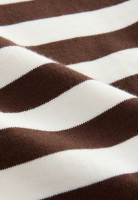 Barna és fehér csíkos kötött anyag, amely puha textúrát és váltakozó széles csíkokat mutat, kiemelve a sima, egyenletes felületet.