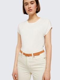 Bijela majica kratkih rukava uparena s lagano bež trapericama i smeđim kožnim remenom. Remen ima zlatnu metalnu kopču i suptilan brend.