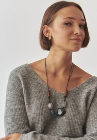 Pulover gri din tricot cu un guler larg. Colierul are perle neregulate în nuanțe de gri, albastru și negru, împletite pe un șnur negru cu accente din lemn.