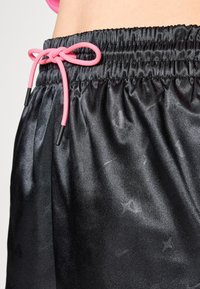 Pantalones cortos de satén negro con un acabado brillante, que cuentan con una cinturilla elástica fruncida de color rosa, con puntas de plástico y patrones de textura sutiles.