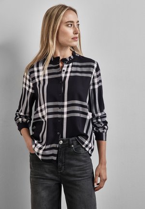 Langärmlige Bluse in schwarz-weißer Karomusterung mit Rüschkragen und Knopfverschluss, kombiniert mit dunkelgrauen Jeans.