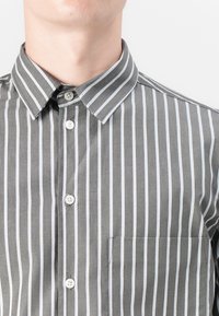 Gray and white striped button-up shirt with a classic collar, a patch pocket, and white buttons on the placket, made from lightweight fabric.