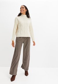 Maglione tortora a collo alto in lavorazione a trecce con dettagli a costine, abbinato a pantaloni a gamba larga con motivo a quadri e décolleté marroni a punta.