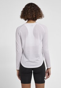 Langærmet, let hvid skjorte med tekstureret stof, bølgerkant og raglanærmer, parret med sorte tætsiddende shorts.