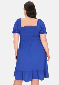 Blaues Kleid mit kurzen Puffärmeln, quadratischem Rückenteil, gerafftem Oberteil und Rüschensaum. Glatte Stoffstruktur, knielanges Design.