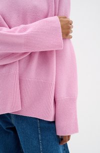 Maglione lavorato a maglia rosa chiaro con polsini e orlo a costine, caratterizzato da una vestibilità comoda e una finitura testurizzata, abbinato a jeans in denim.