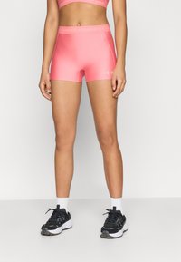 Ροζ σορτς συμπίεσης από λείο, ελαστικό ύφασμα με λωρίδα λογότυπου. Συνδυάζονται με μαύρα αθλητικά παπούτσια και λευκές κάλτσες.