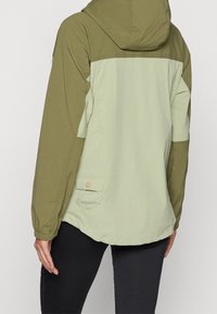 Chaqueta verde claro y oliva con capucha, puños elásticos y un bolsillo en la parte posterior, fabricada con un tejido ligero y suave.