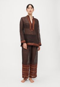 Mustast läbipaistvast kangast tuunika V-kaelusega ja oranži triibulise mustriga, sobitatud lahtiste pükstega, millel on sarnased triibud.