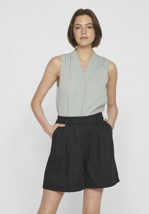 Blouse sans manches gris clair avec un décolleté en V, associée à un short noir taille haute avec des plis et des poches latérales.