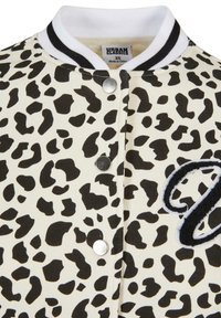 Veste imprimé léopard avec col côtelé rayé noir et blanc, boutons-pression argentés et écusson lettre texturé noir et blanc sur la poitrine.