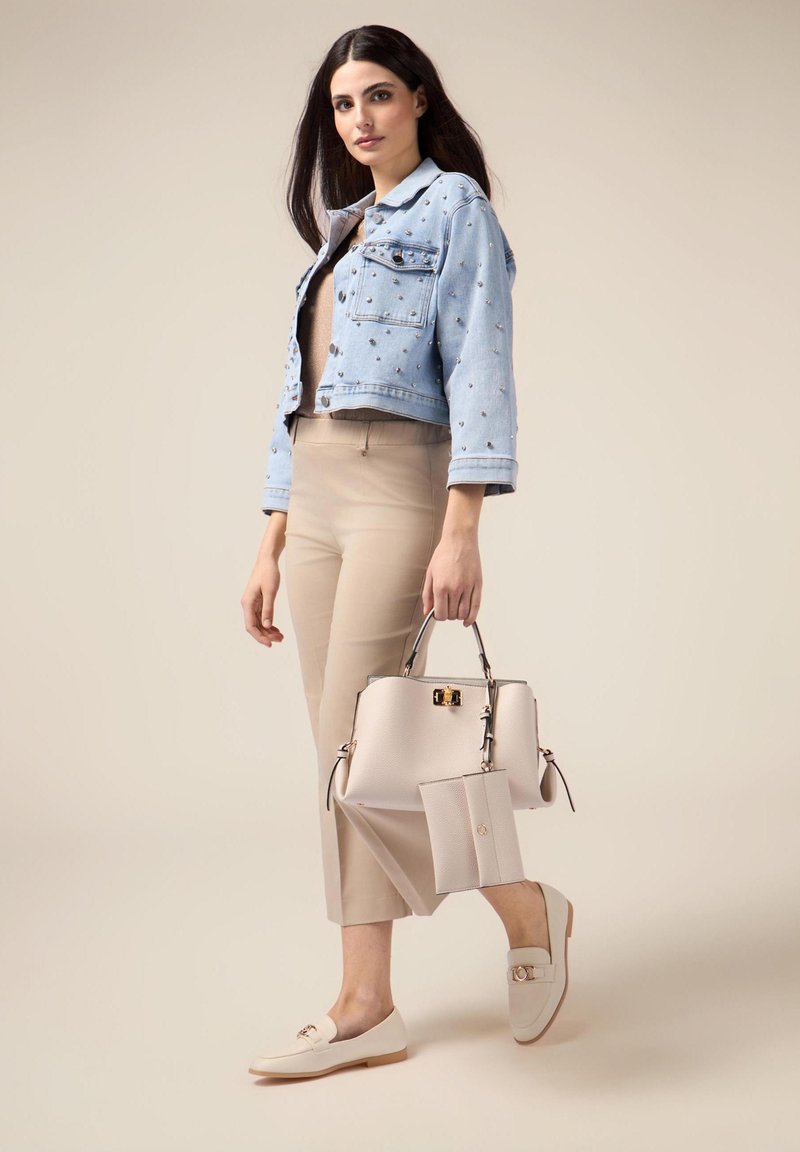 Ljusblå kort denimjacka med utsmyckningar, beige figurnära byxor, krämfärgad handväska med gulddetaljer och matchande loafers.