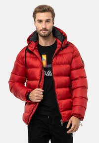Rote Puffer-Jacke mit schwarzem Kapuzen, Reißverschluss vorne, elastischen Bündchen und einer gesteppten Textur. Kombiniert mit einem schwarzen T-Shirt mit einem bunten Logo.