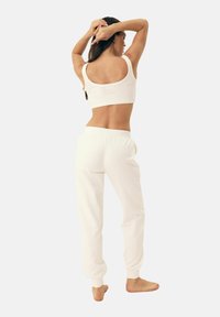 Biała bluzka crop i pasujące dresy wykonane z miękkiej tkaniny. Posiada okrągły dekolt, elastyczny pas i zwężane mankiety.