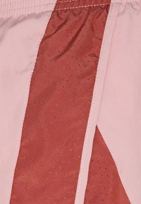 Light pink shorts feature a panel of textured rust fabric with small perforations, stitched edges, and a waistband with elastic.