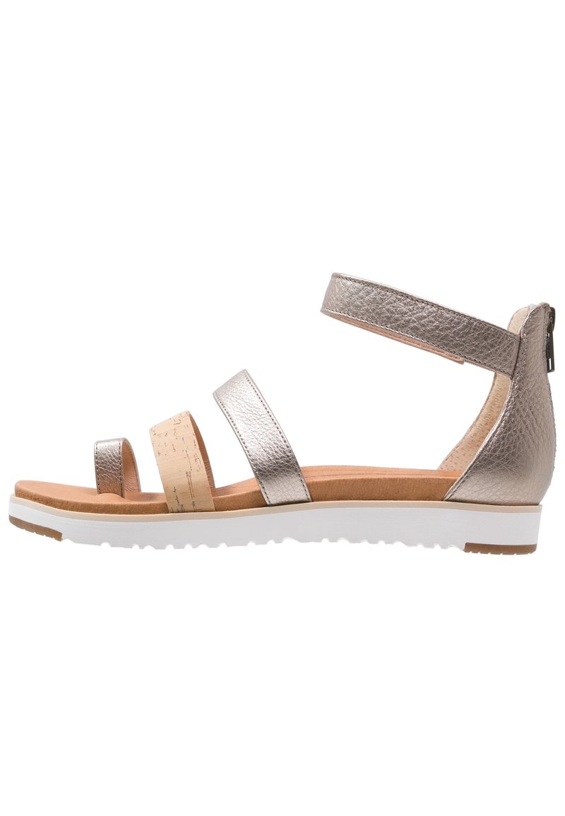 Płaskie sandały z metallicznymi skórzanymi paskami, korkowym akcentem, paskiem na kostkę z zamkiem oraz wyściełanym brązowym wkładem na białej podeszwie.