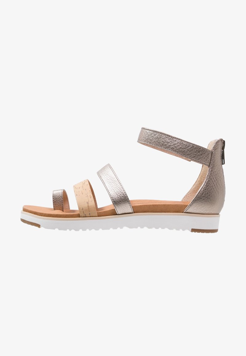 Płaskie sandały z metallicznymi skórzanymi paskami, korkowym akcentem, paskiem na kostkę z zamkiem oraz wyściełanym brązowym wkładem na białej podeszwie.