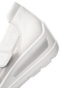White sneakers featuring a smooth leather upper, elastic panel, textured detailing, and a thick sole with a clear accent.