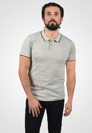 Siva pletena polo majica s crnim detaljima, s tri gumba, kratkim rukavima i teksturiranim uzorkom. Nošena s crnim hlačama.