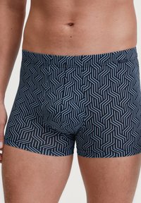 Marineblauwe boxershorts met een geometrisch wit patroon, gemaakt van rekbaar materiaal. Kenmerkt zich door een comfortabele tailleband en een nauwsluitend ontwerp.